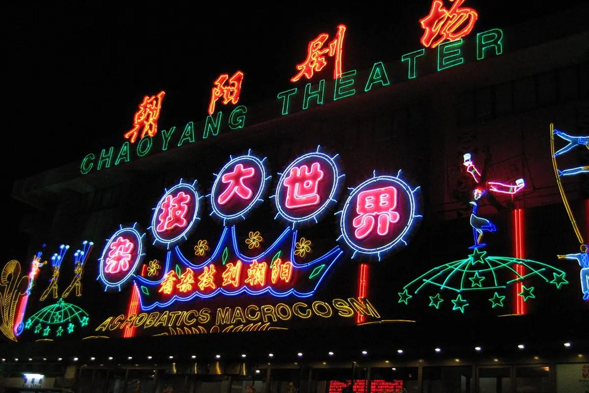 The Chaoyang Theater front at night, with its neon sign in English and Chinese and neon figures of acrobats on either side